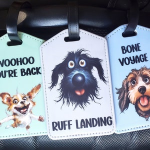 May include: Three luggage tags with dog illustrations and funny sayings. The first tag is green with a brown and white dog and the text "Woohoo You're Back". The second tag is white with a black dog and the text "Ruff Landing". The third tag is blue with a brown and white dog and the text "Bone Voyage".
