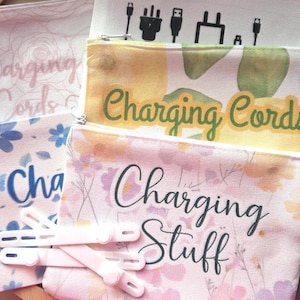 May include: Several zippered pouches with floral and botanical patterns. The pouches have text that reads "Charging Cords" and "Charging Stuff". Pink cable organizers are in the foreground. The pouches are designed to store charging accessories.