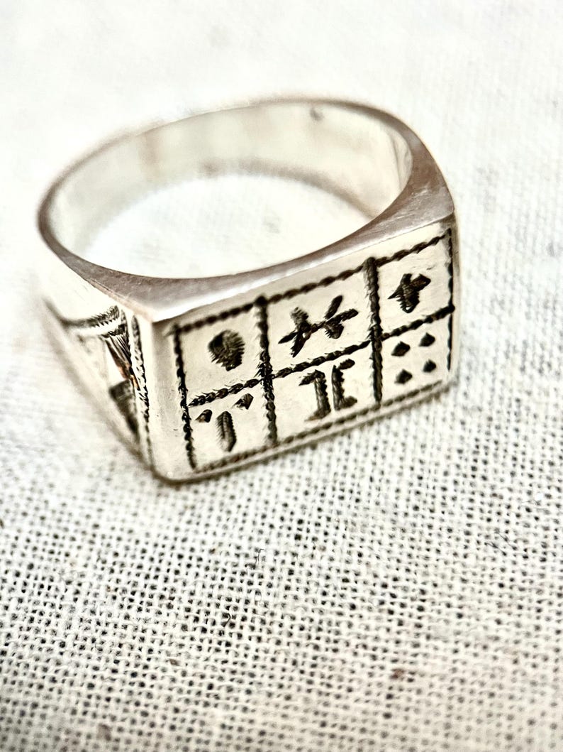 Puede incluir: Un anillo de plata con un dise&ntilde;o cuadrado que presenta un patr&oacute;n de s&iacute;mbolos y puntos.