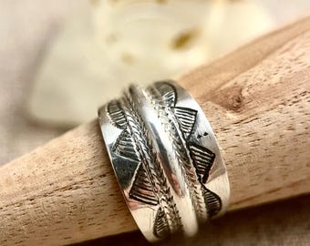 Könnte beinhalten: Ein silberner Ring mit geometrischem Muster. Der Ring ist breit und hat eine strukturierte Oberfläche.