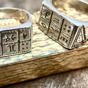 Puede incluir: Dos anillos de plata con intrincados dise&ntilde;os grabados. Los anillos son de forma cuadrada y presentan patrones geom&eacute;tricos.