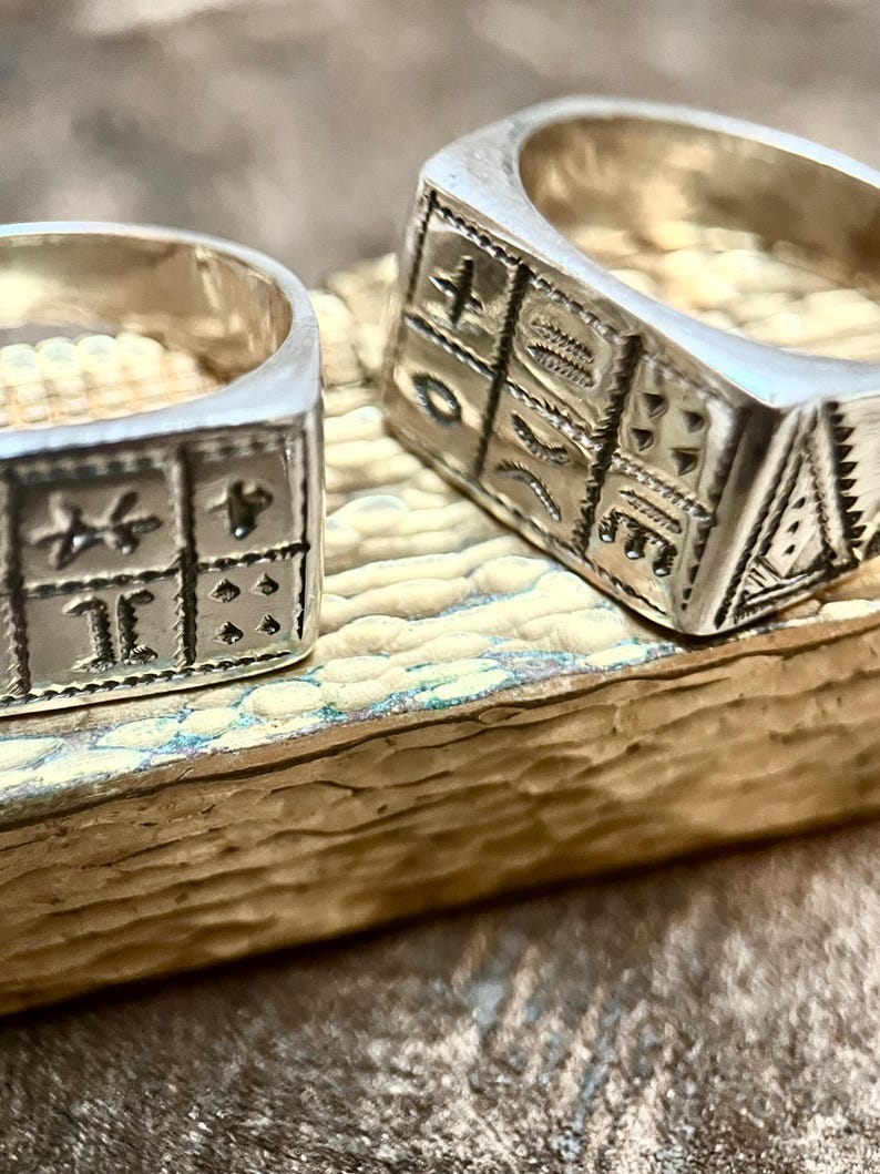 Puede incluir: Dos anillos de plata con intrincados dise&ntilde;os grabados. Los anillos son de forma cuadrada y presentan patrones geom&eacute;tricos.