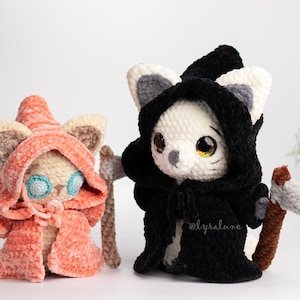 May include: Two crocheted cat plushies dressed in costumes. One is wearing a red hooded robe and the other is wearing a black hooded robe with a scythe.