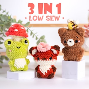 Pode incluir: Três padrões de amigurumi de crochê: um sapo verde com um cogumelo vermelho e branco, um urso marrom com uma abelha amarela e uma raposa laranja com uma flor rosa. O padrão se chama "3 em 1 Low Sew".