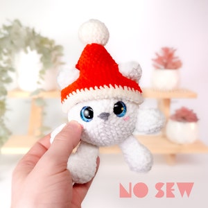 Könnte beinhalten: Weißes gehäkeltes Plüschtier, das einen roten gehäkelten Weihnachtsmann-Hut mit einem weißen Bommel trägt. Das Spielzeug hat große blaue Augen und eine rosa Nase. Der Text "NO SEW" ist unten im Bild sichtbar.