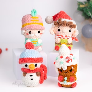 Könnte beinhalten: Vier handgefertigte gehäkelte Weihnachtsschmuckstücke. Die Ornamente umfassen einen Nussknacker, einen Elfen, einen Schneemann und einen Lebkuchenmann. Die Ornamente sind weiß, rot, blau, rosa und braun. Die Ornamente befinden sich auf einer weißen Oberfläche.