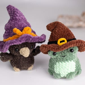 May include: Two handmade crochet plushies: a brown bird and a green frog, both wearing witch hats. The bird's hat is purple with an orange bow, and the frog's hat is brown with a yellow buckle. These whimsical toys are perfect for Halloween.