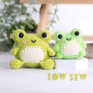 May include: Two crocheted green frog plushies with white accents. The larger frog is sitting on a white surface with the text "LOW SEW" in yellow.