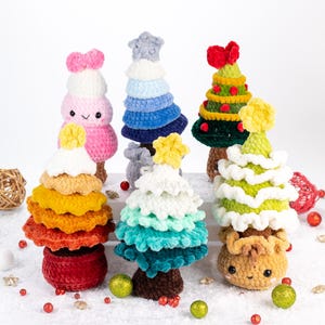 Könnte beinhalten: Sechs gehäkelte Weihnachtsbäume in verschiedenen Farben und Stilen. Die Bäume sind in einem Halbkreis auf einer weißen Oberfläche angeordnet.