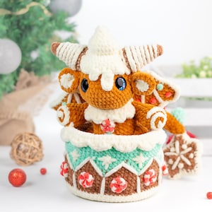 May include: A crocheted gingerbread house toy with a brown and white gingerbread character inside. The house is decorated with candy canes and white frosting. The character has a white frosting hat and brown eyes.
