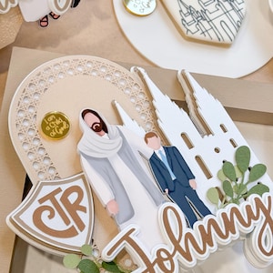 May include: A brown and white cake topper with a white temple, a white figure of Jesus Christ, a white figure of a man in a suit, and the text "CTR" and "Johnny".