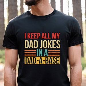 May include: A black t-shirt with a vintage-style graphic that reads "I keep all my dad jokes in a dad-a-base".