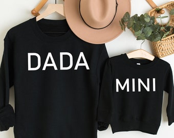 Könnte beinhalten: Zwei schwarze Sweatshirts mit weißem Text. Das größere Sweatshirt sagt "DADA" und das kleinere Sweatshirt sagt "MINI".