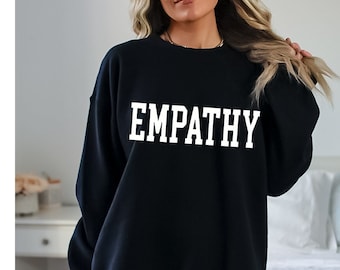 Könnte beinhalten: Schwarzer Pullover mit dem Wort "EMPATHY" in weiß auf der Vorderseite.