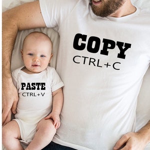 May include: A white t-shirt with the text "COPY CTRL+C" on it. A baby is wearing a white onesie with the text "PASTE CTRL+V" on it.