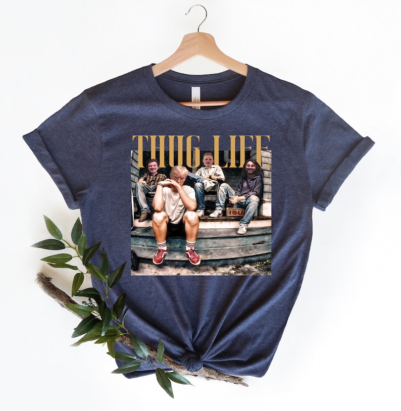 May include: Navy blue t-shirt with a graphic of four people sitting on a porch. The graphic includes the text "THUG LIFE" in gold letters.