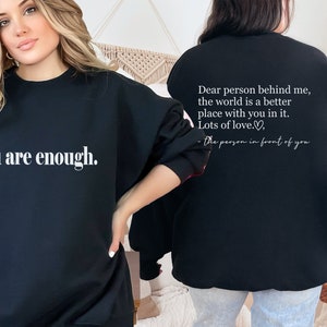 May include: Black sweatshirt with the text "you are enough." on the front and the text "Dear person behind me, the world is a better place with you in it. Lots of love. - the person in front of you" on the back.