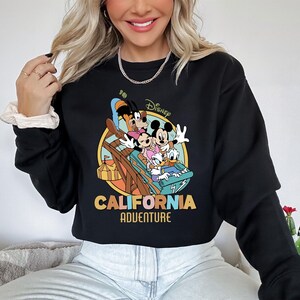 May include: Black sweatshirt featuring a colorful graphic of Disney characters on a ride, with the words "Disney California Adventure" in a retro font. The sweatshirt is a crew neck style.