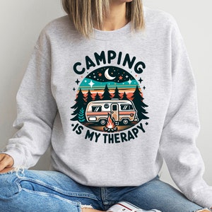 Op de afbeelding: Grijs sweatshirt met een retro-grafiek van een camper in een bosrijke omgeving. De tekst luidt "Camping is my therapy."