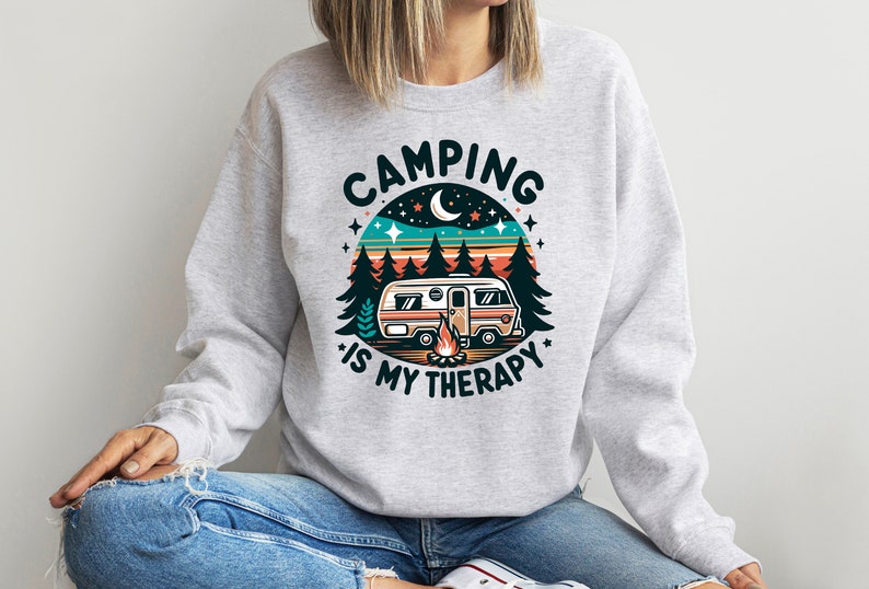 Op de afbeelding: Grijs sweatshirt met een retro-grafiek van een camper in een bosrijke omgeving. De tekst luidt "Camping is my therapy."