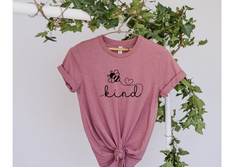 May include: A pink t-shirt with a black bee graphic and the word "kind" printed on it. The bee is flying with a heart behind it.
