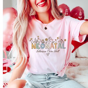 May include: A pink t-shirt with the text "NEONATAL Intensive Care Unit" in colorful letters with a small heart in the middle of the word "NEONATAL". The letters are surrounded by small flowers.