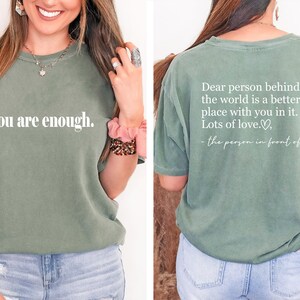 Pu&ograve; includere: Una maglietta verde con la scritta "you are enough." sul davanti e la scritta "Dear person behind me, the world is a better place with you in it. Lots of love. - the person in front of you" sul retro.