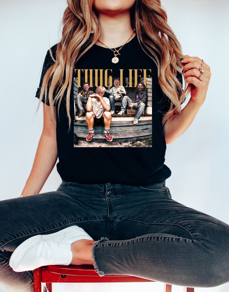 May include: Black t-shirt with a graphic print of four people sitting on a porch. The text "THUG LIFE" is printed in gold letters above the image.