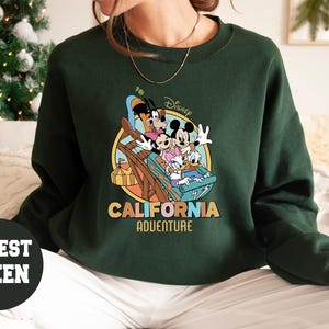 May include: Forest green sweatshirt featuring a colorful graphic of Disney characters on a ride, with the words "California Adventure" in a retro font. The sweatshirt is a crew neck style.