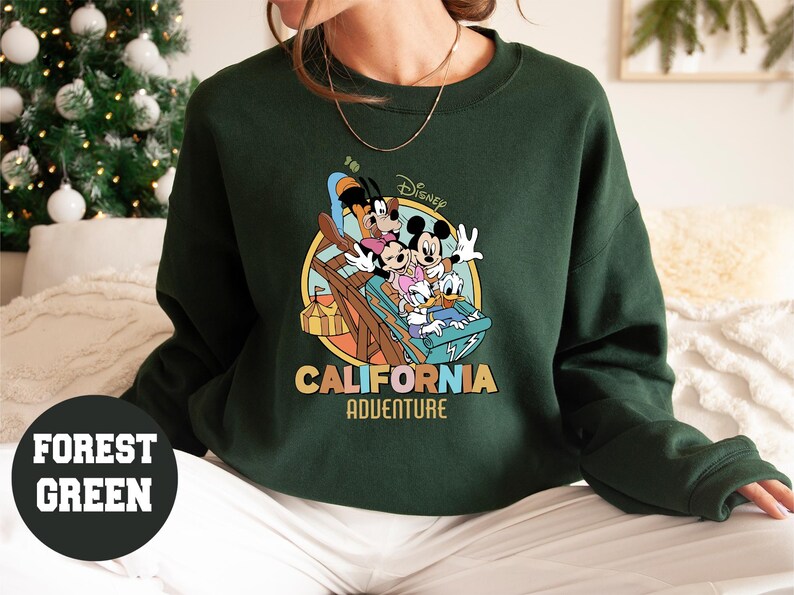 May include: Forest green sweatshirt featuring a colorful graphic of Disney characters on a ride, with the words "California Adventure" in a retro font. The sweatshirt is a crew neck style.
