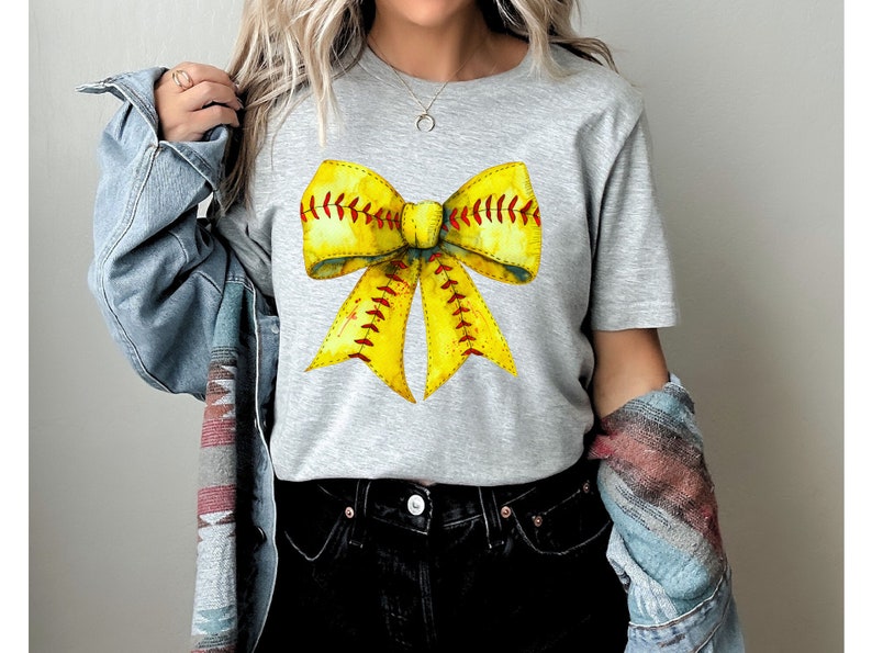 K&ouml;nnte beinhalten: Ein graues T-Shirt mit einem gelben und roten Softball-Schleifendesign. Die Schleife ist so gestaltet, dass sie einem Softball mit roten N&auml;hten &auml;hnelt.