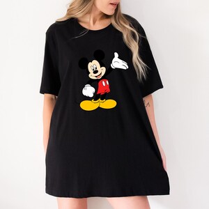 Puede incluir: Camiseta negra con un gr&aacute;fico de Mickey Mouse. El personaje de dibujos animados se muestra con una mano enguantada blanca levantada, pantalones cortos rojos y zapatos amarillos. La camiseta es de estilo holgado y de gran tama&ntilde;o.