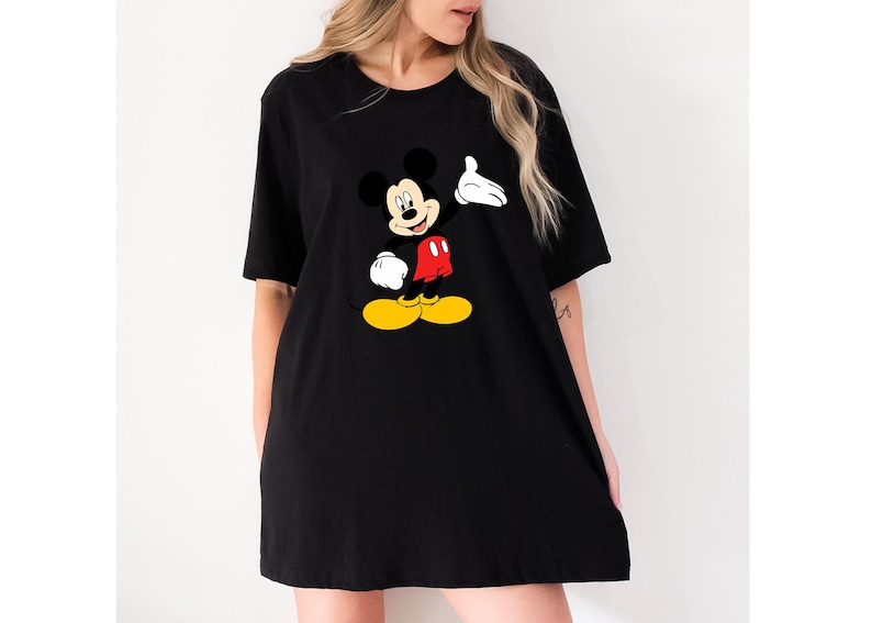 Puede incluir: Camiseta negra con un gr&aacute;fico de Mickey Mouse. El personaje de dibujos animados se muestra con una mano enguantada blanca levantada, pantalones cortos rojos y zapatos amarillos. La camiseta es de estilo holgado y de gran tama&ntilde;o.