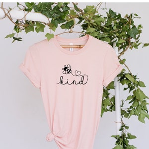 May include: A pink t-shirt with a black bee and heart design and the word "kind" printed on it.