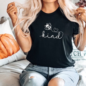May include: Black t-shirt with a white bee and flower graphic and the text "be kind" in a cursive font.