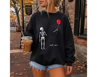 Könnte beinhalten: Ein schwarzes Sweatshirt mit Rundhalsausschnitt und einer Grafik eines weißen Skeletts, das einem wegfliegenden roten Luftballon nachsieht, wobei eine Skeletthand nach der Schnur greift und der Text "Well, shit..." weiß unter dem Ballon steht.