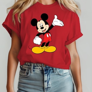 Puede incluir: Camiseta roja con un dibujo de Mickey Mouse. El personaje de dibujos animados tiene orejas negras, cuerpo negro, pantalones cortos rojos, zapatos amarillos y guantes blancos. La camiseta tiene mangas enrolladas.
