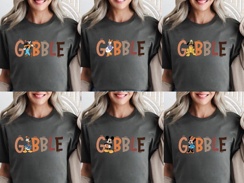 May include: A dark gray t-shirt with the word "GOBBLE" in orange and brown letters. Each letter features a different cartoon character, including Goofy, Donald Duck, Pluto, Daisy Duck, Mickey Mouse, and Minnie Mouse.