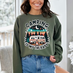 Op de afbeelding: Groen sweatshirt met een retro-grafische afbeelding van een camper in een bos met de tekst "Camping is my therapy".