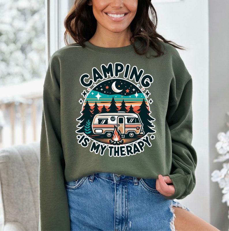 Op de afbeelding: Groen sweatshirt met een retro-grafische afbeelding van een camper in een bos met de tekst "Camping is my therapy".