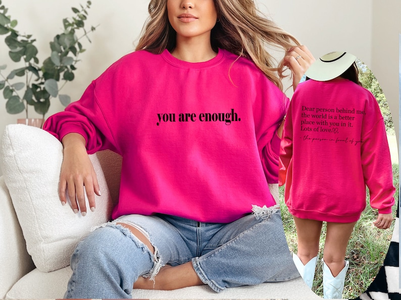 May include: A bright pink sweatshirt with the text "you are enough." printed on the front. The back of the sweatshirt has the text "Dear person behind me, the world is a better place with you in it. Lots of love." printed on it.