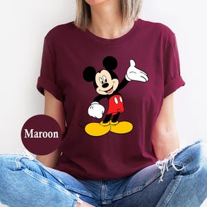 Puede incluir: Camiseta granate con un gr&aacute;fico de Mickey Mouse. Mickey se muestra con orejas negras, cuerpo negro, guantes blancos, pantalones cortos rojos y zapatos amarillos. La camiseta es de color granate liso.