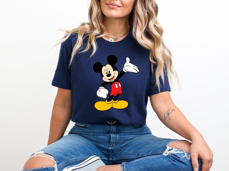 Puede incluir: Camiseta azul marino con un dise&ntilde;o de Mickey Mouse. El personaje de dibujos animados se representa con orejas negras, pantalones cortos rojos, zapatos amarillos y guantes blancos. La camiseta es de cuello redondo.