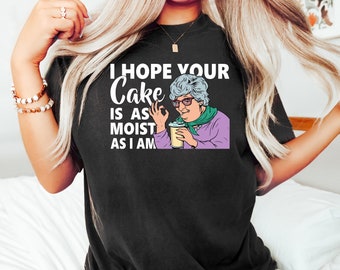 May include: Black t-shirt with a white graphic of a woman holding a drink and saying "I hope your cake is as moist as I am."