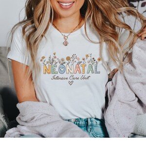 May include: White t-shirt with a floral design and the text "NEONATAL Intensive Care Unit" in colorful letters with a blue heart.