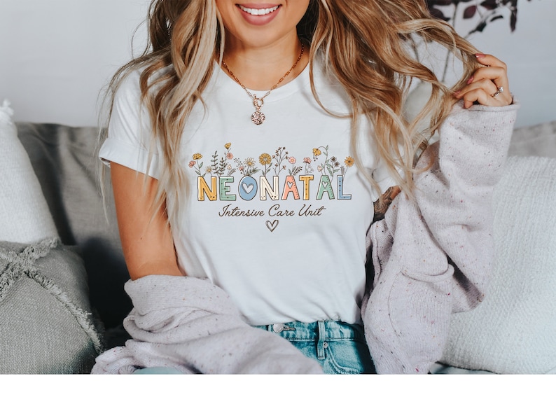 May include: White t-shirt with a floral design and the text "NEONATAL Intensive Care Unit" in colorful letters with a blue heart.