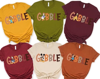 May include: Six colorful t-shirts in mustard yellow, olive green, burgundy, beige, rust, and maroon. Each shirt features the word "GOBBLE" in a fall-themed font, with a different cartoon character illustration.