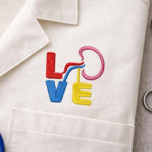 May include: White medical coat with an embroidered design spelling "LOVE". The letters are in red, blue, yellow, and pink. A stethoscope and surgical scissors are visible in the background.
