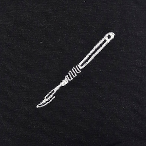 Op de afbeelding: Zwarte stof met een wit geborduurd scalpelontwerp. Het scalpel is weergegeven in een gedetailleerde, realistische stijl, met een gebogen mes en een getextureerde handgreep. De borduursels zijn netjes en precies.