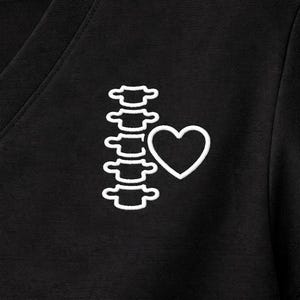 May include: Black V-neck shirt with a white embroidered design of a spine and a heart. The design is located on the left side of the shirt. The shirt is made of a soft, dark fabric.